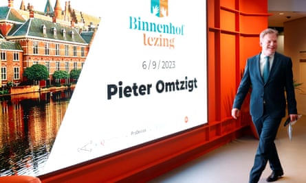 Smiling Dutch politician Pieter Omtzigt walks by a poster that reads reads the Binnenhof Lezing Pieter Omtzigt