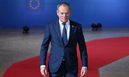 Donald Tusk standing with squared shoulders on a red carpet with an EU-themed backdrop behind him
